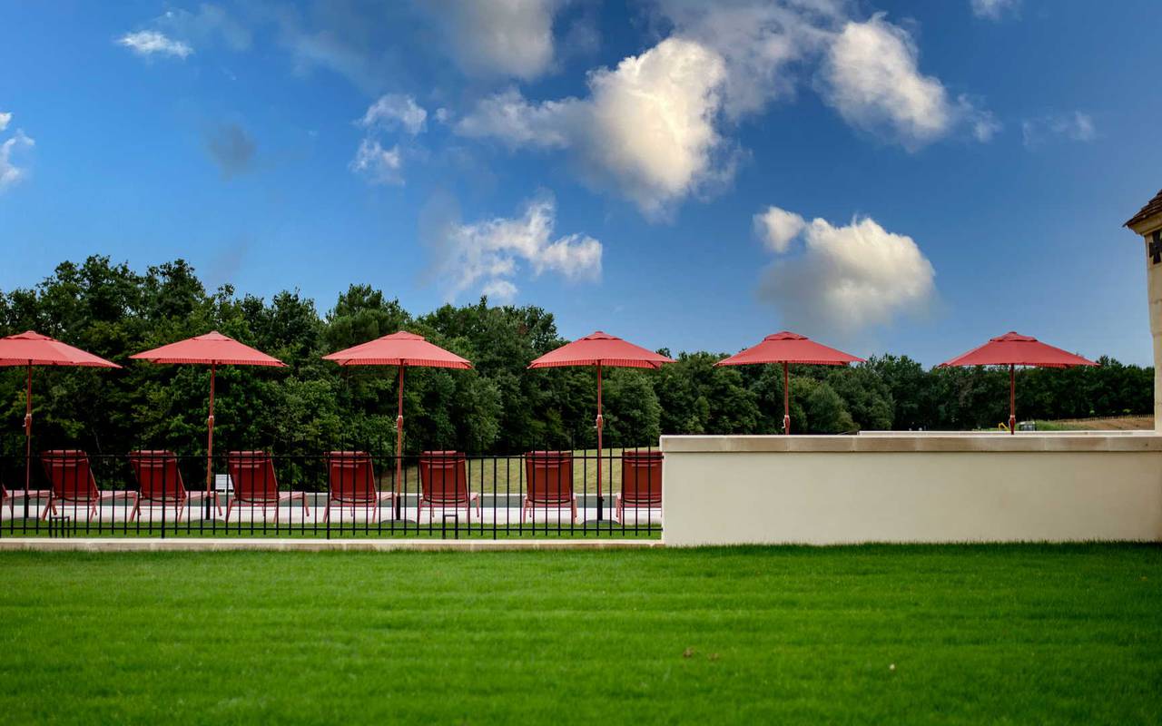 Vue sur les parasols rouges, le ciel bleu et la belle herbe verte de notre hôtel proposant un hébergement insolite dans la région de Saint Emilion- Château Fage 